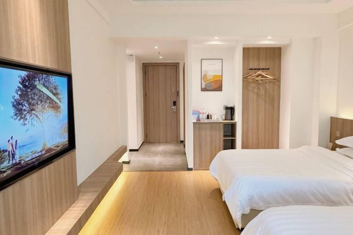 Ein modernes Hotelzimmer mit Fernseher an der Wand, Holzboden, Bett, kleinem Schreibtisch und Kleiderschrank.