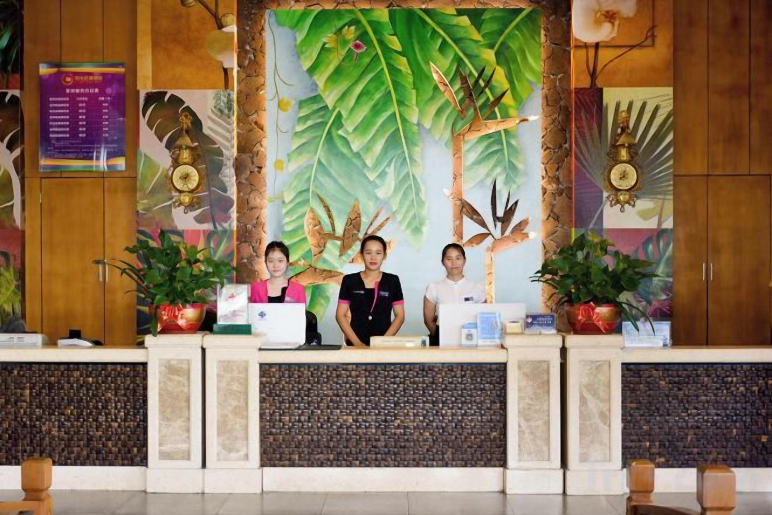 Una recepción con tres empleados, un gran mural con temática tropical y plantas en macetas.