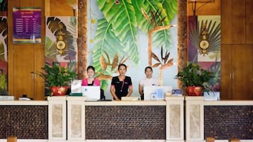 Una recepción con tres empleados, un gran mural con temática tropical y plantas en macetas.