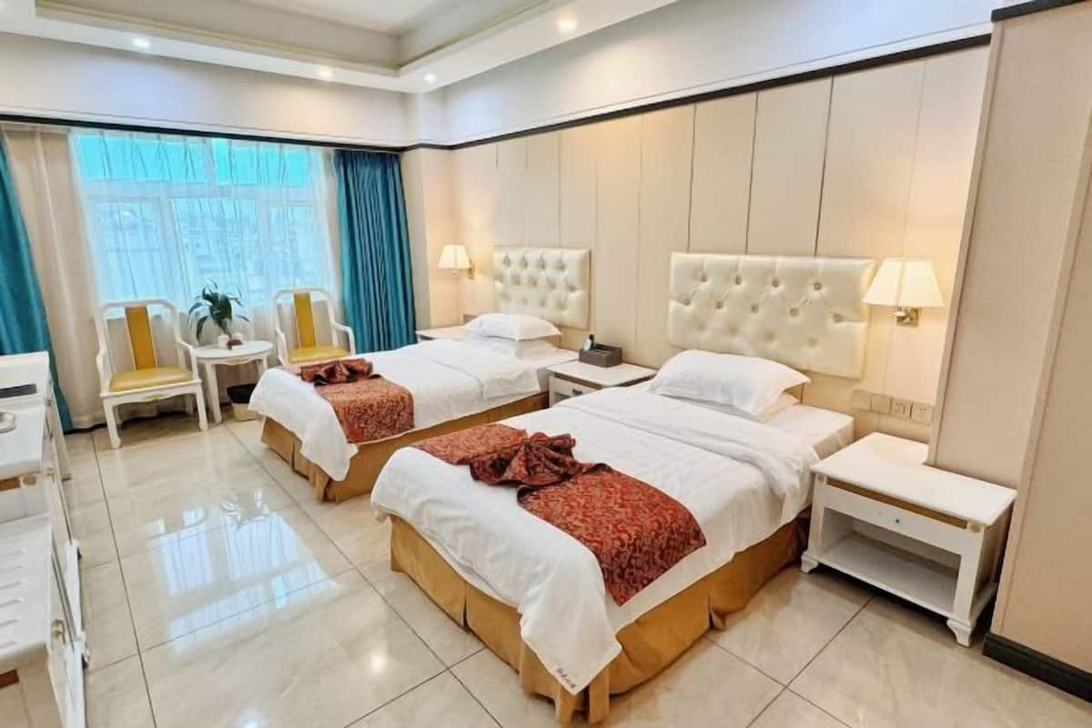 Ein Hotelzimmer mit zwei Betten, einem kleinen Tisch, Stühlen und einem fensterbelagten Fenster.