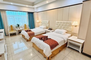 Habitación de hotel con dos camas, una mesita, sillas y un ventanal con cortinas.