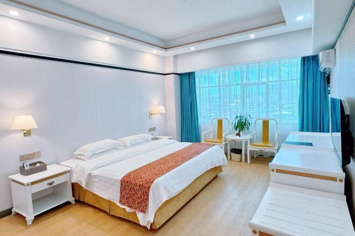 Ein Hotelzimmer mit einem Bett, Nachttischen, einem Sessel, einem kleinen Tisch und einem Fernseher.