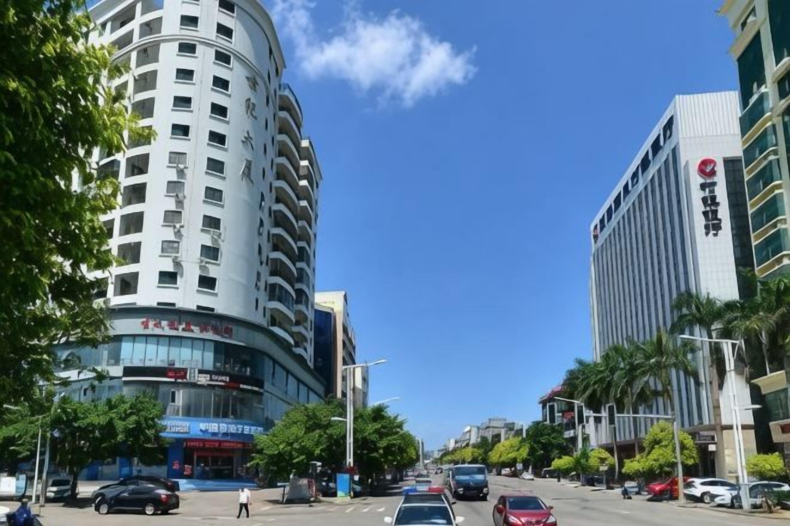A multi-story building with a curved facade, a clear blue sky, and a street with parked cars and palm trees.
