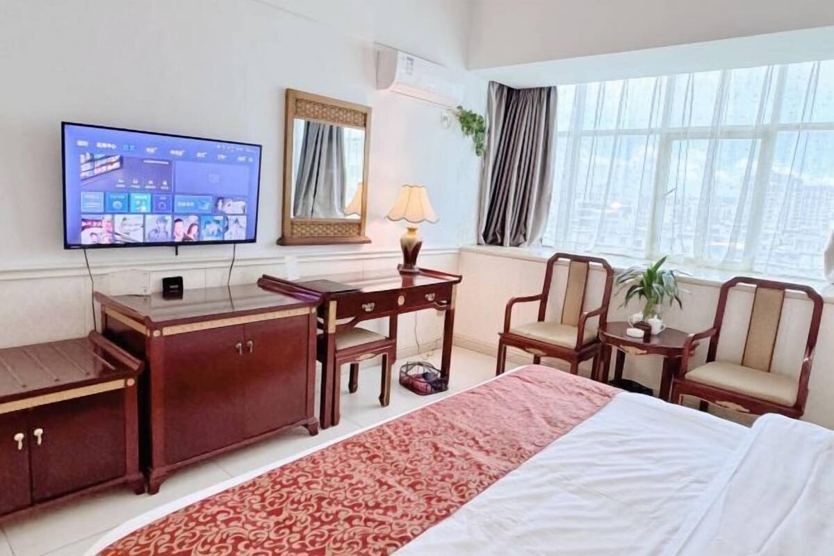 Ein Hotelzimmer mit Bett, Schreibtisch, Stühlen, einem Fernseher und einem Fenster mit Vorhängen.