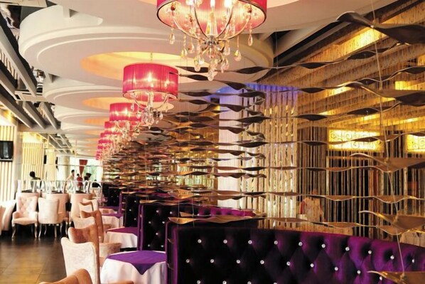 A restaurant with rows of tables and chairs, a patterned wall, and a chandelier. - Yangguang Yihao Hotel (Qionghai)