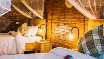 A room with a brick wall, a bed with white bedding, a nightstand with a lamp, and a canopy bed with a patterned canopy.