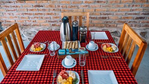 A breakfast table set with plates of fruit, a coffee pot, and a bottle of water. - Rafiki Retreat (Arusha)
