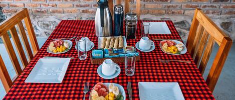 A breakfast table set with plates of fruit, a coffee pot, and a bottle of water.