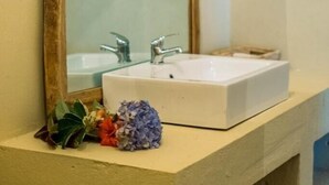 A bathroom with a white sink, two faucets, a wooden-framed mirror, and a small plant on the counter. - Rafiki Retreat (Arusha)