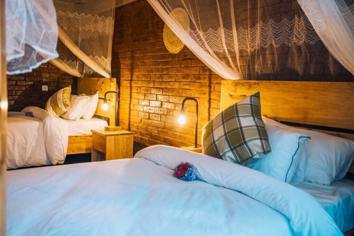 A cozy bedroom with a brick wall, two beds with white bedding, wooden nightstands, and a canopy bed with a decorative hanging.