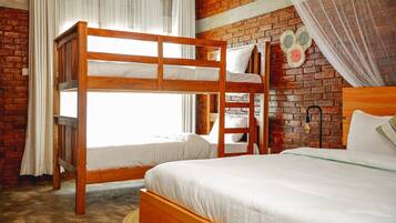 Una habitación con dos literas, una cama individual, una pared de ladrillo, una ventana con cortinas y una lámpara fijada a la pared.