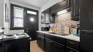A kitchen with black cabinets, a stove, a sink, and a brick backsplash. - Merion Village Residences 1166 (Columbus)