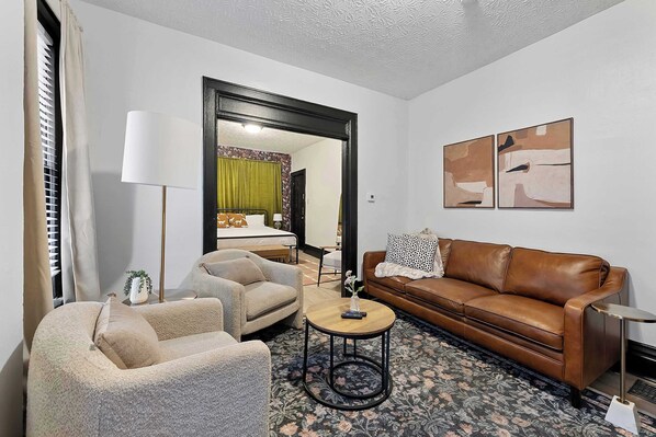 A living room with a brown leather sofa, beige armchair, and a round coffee table. A floral rug covers the floor. - Merion Village Residences 1166 (Columbus)