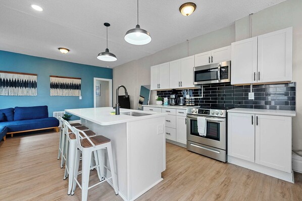 A modern kitchen with white cabinets, stainless steel appliances, and a central island with bar stools. - Merion Village Residences 1166.5 (Columbus)