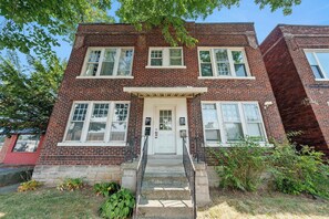 A two-story brick building with a white front door, multiple windows, and a small porch with a railing. - Merion Village Residences 1166.5 (Columbus)