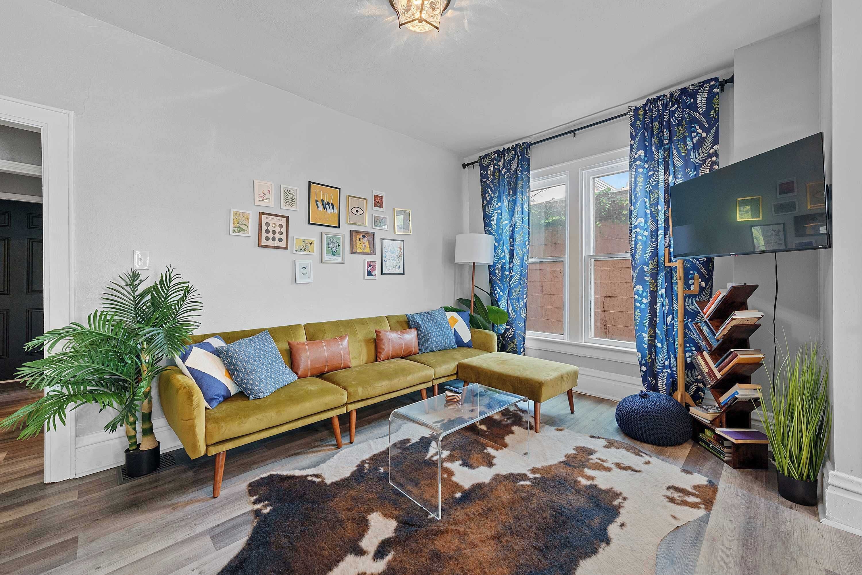 A living room with a green sofa, a glass coffee table, a cowhide rug, and a bookshelf.