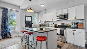 A modern kitchen with white cabinets, stainless steel appliances, and a central island with stools. - Merion Village Residences Suites (Columbus)
