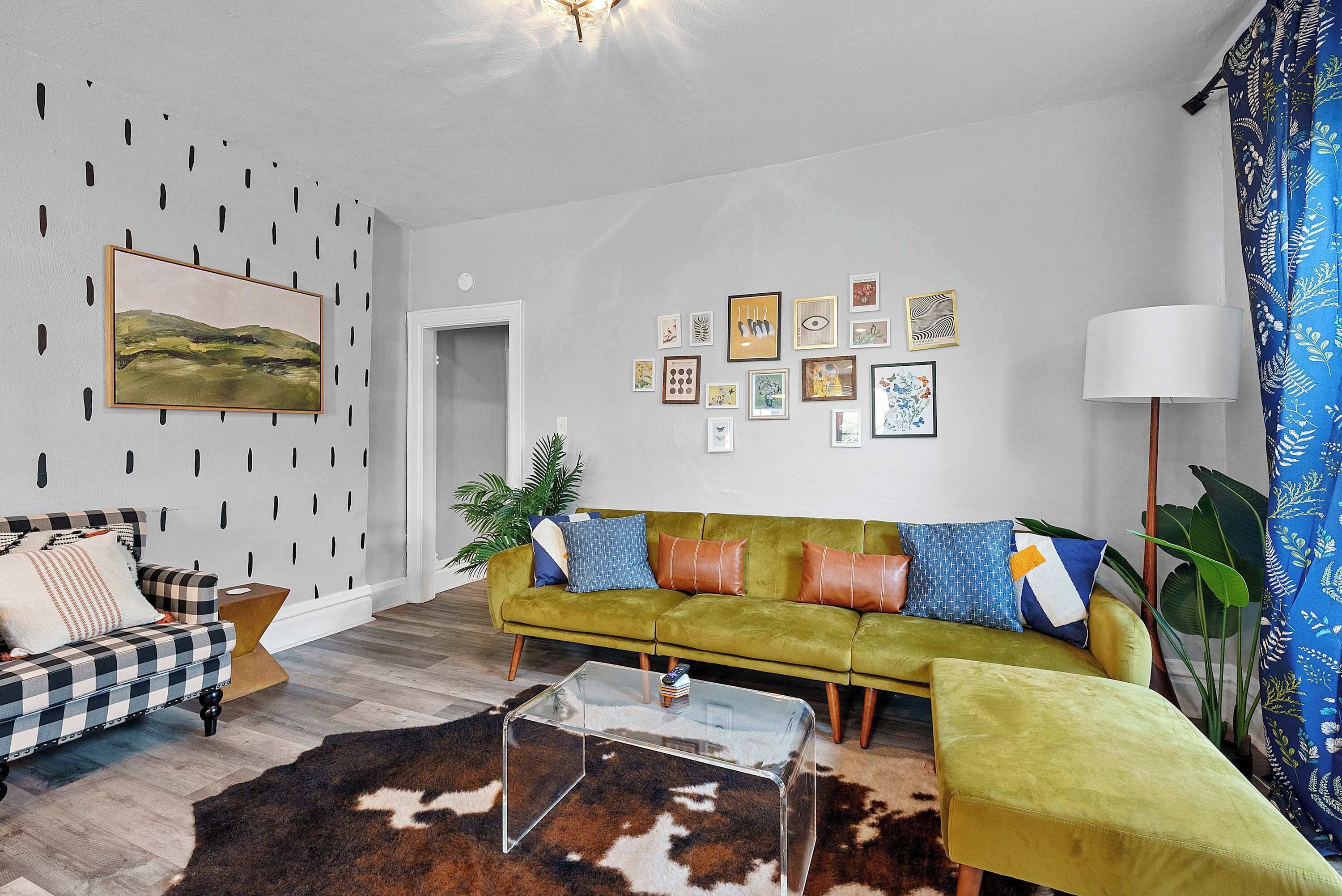 Ein Wohnzimmer mit einem grünen Sofa, einem karierten Sofa, einem Glastisch und einem Cowhide-Teppich.