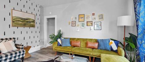 A living room with a green sofa, a checkered sofa, a glass coffee table, and a cowhide rug.