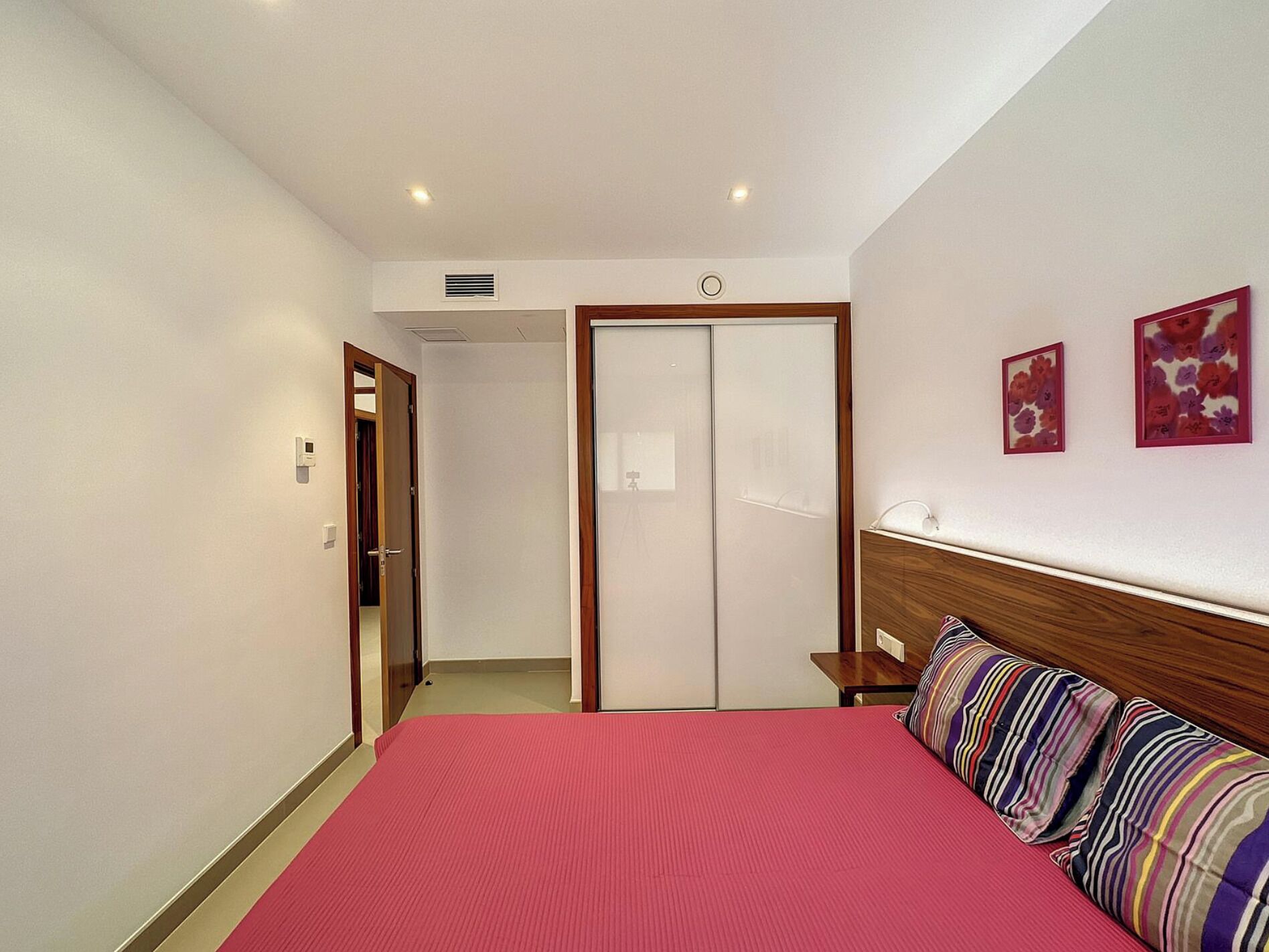 A hotel room with a bed, a wooden headboard, a wardrobe, and two framed pictures on the wall.