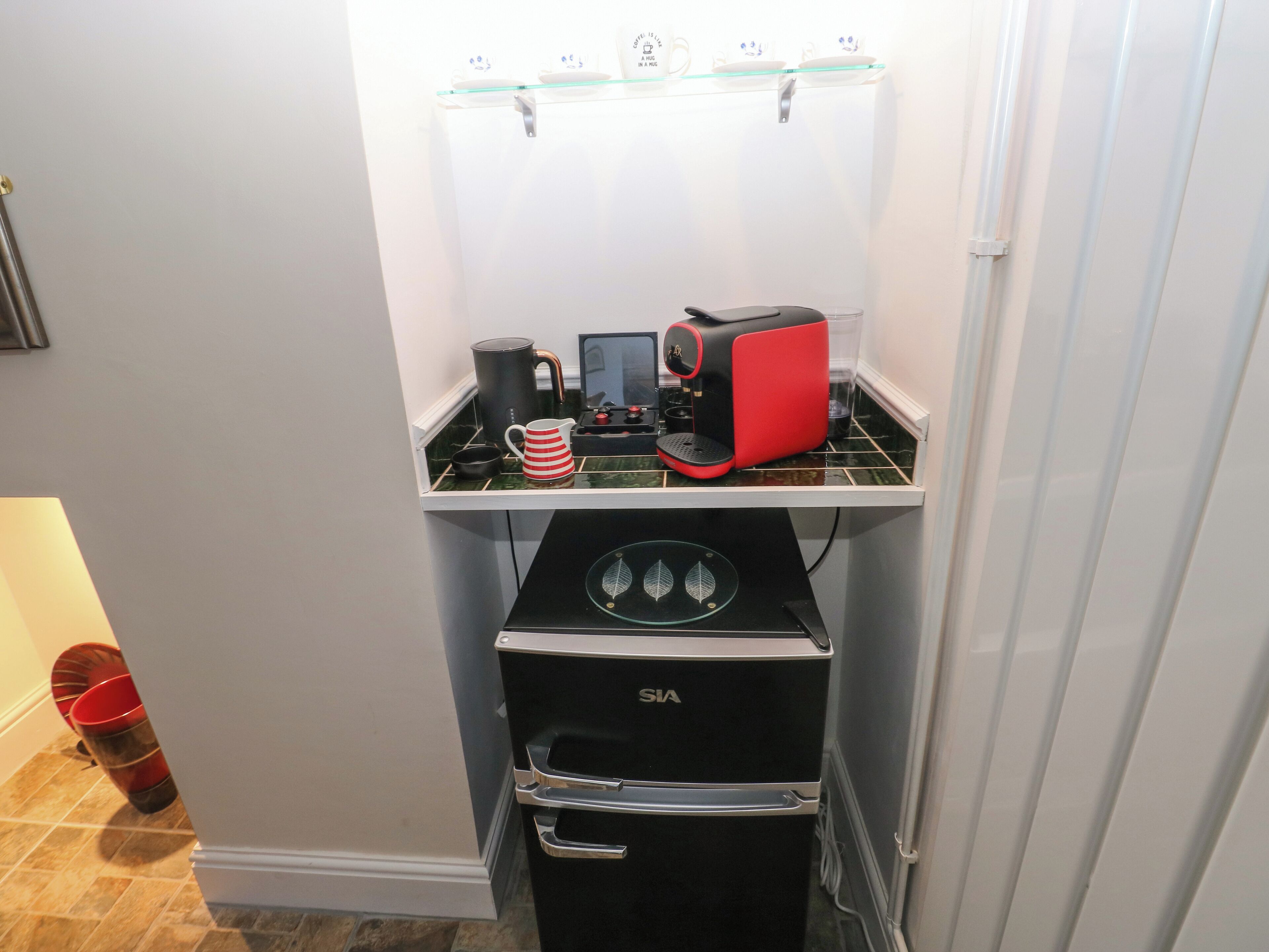 A compact kitchenette with a coffee maker, kettle, and a small refrigerator.