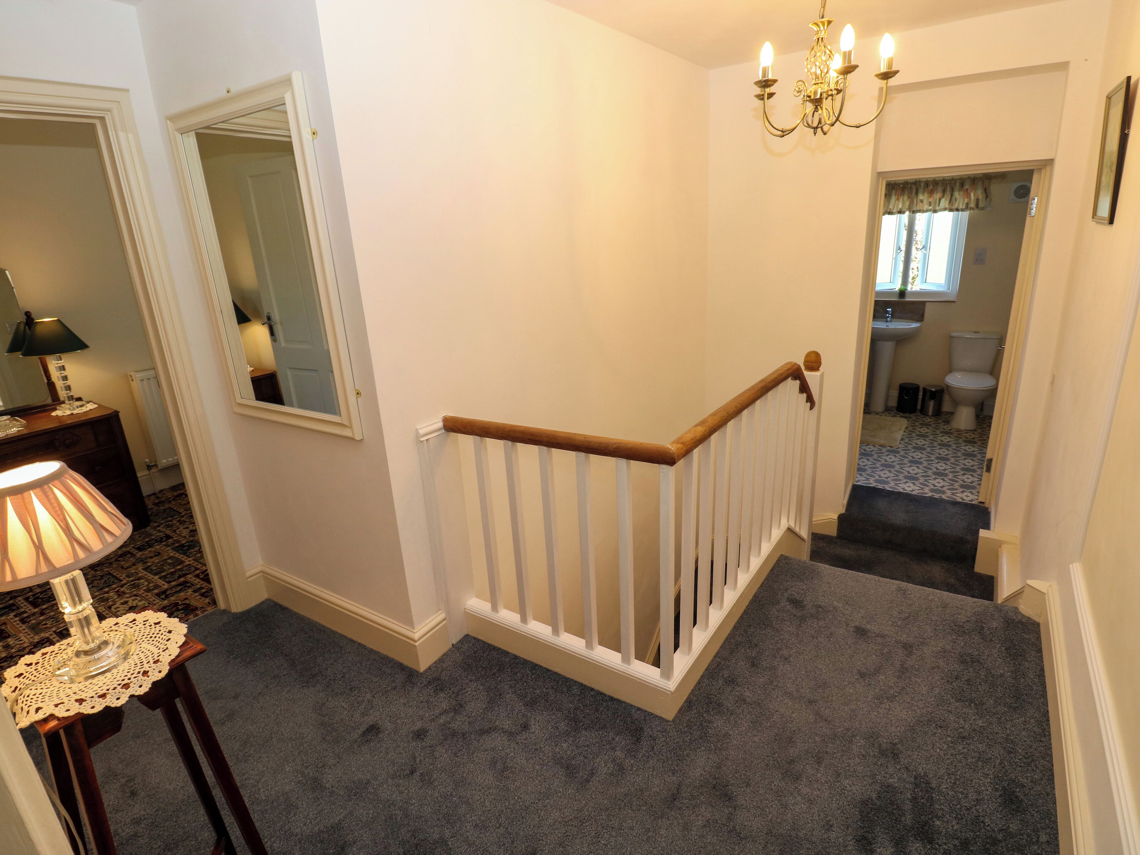 A staircase with a white railing, carpeted steps, and a chandelier.