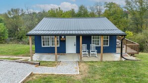 A small, single-story building with a blue exterior and a metal roof, featuring a front porch with two white chairs and a wooden deck. - The Ark Encounter Getaway (Williamstown)