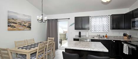 A modern kitchen with a marble island, black cabinets, and a dining area with a checkered tablecloth.