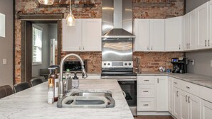 Una cucina moderna con mobili bianchi, una cappa in acciaio inossidabile e un parete in mattoni.