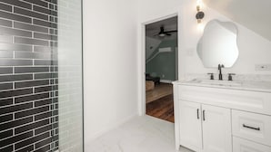 Un baño con tocador blanco, un espejo grande y una zona de ducha con azulejos negros.
