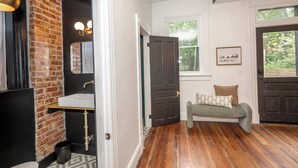 Una habitación con pared de ladrillo, un lavamanos blanco, un banco de madera y una puerta que da al exterior.