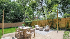 Un patio al aire libre con piso de concreto, rodeado por una valla de madera y abundante vegetación.