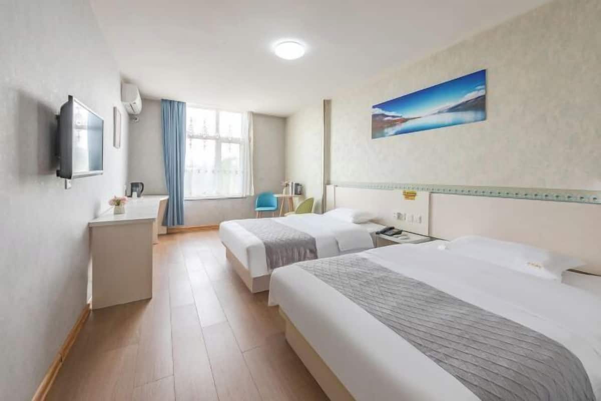 A hotel room with two beds, a desk, a chair, a TV, and a window with curtains.