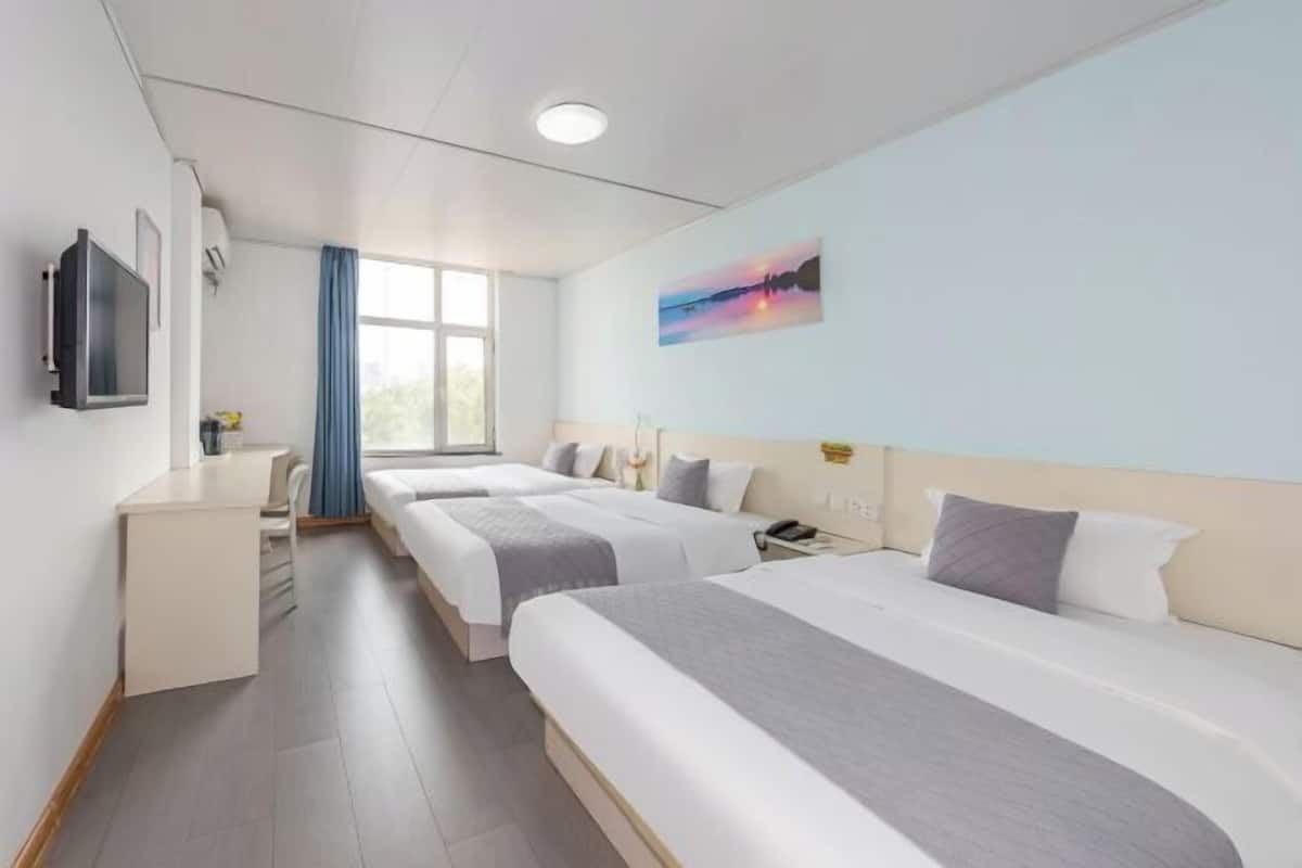 A hotel room with two beds, a desk, a TV, and a painting on the wall.