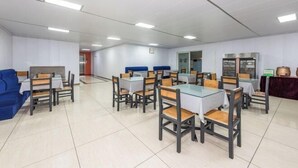 A dining area with tables and chairs, a blue sofa, and a kitchen area with a stove and refrigerator.