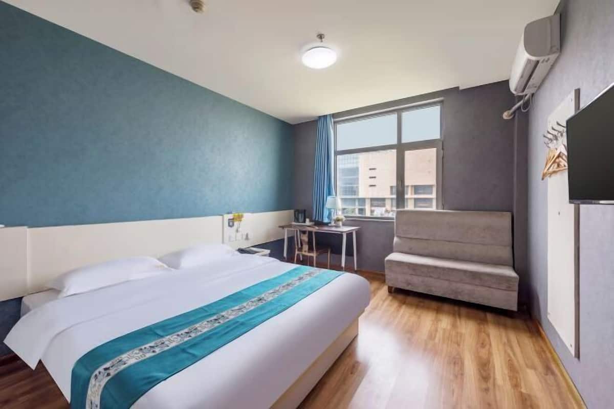 A hotel room with a bed, a desk, a chair, and a window with a view of buildings.