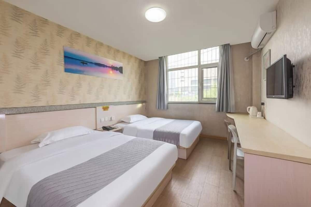 A hotel room with two beds, a TV, a window with curtains, and a painting on the wall.