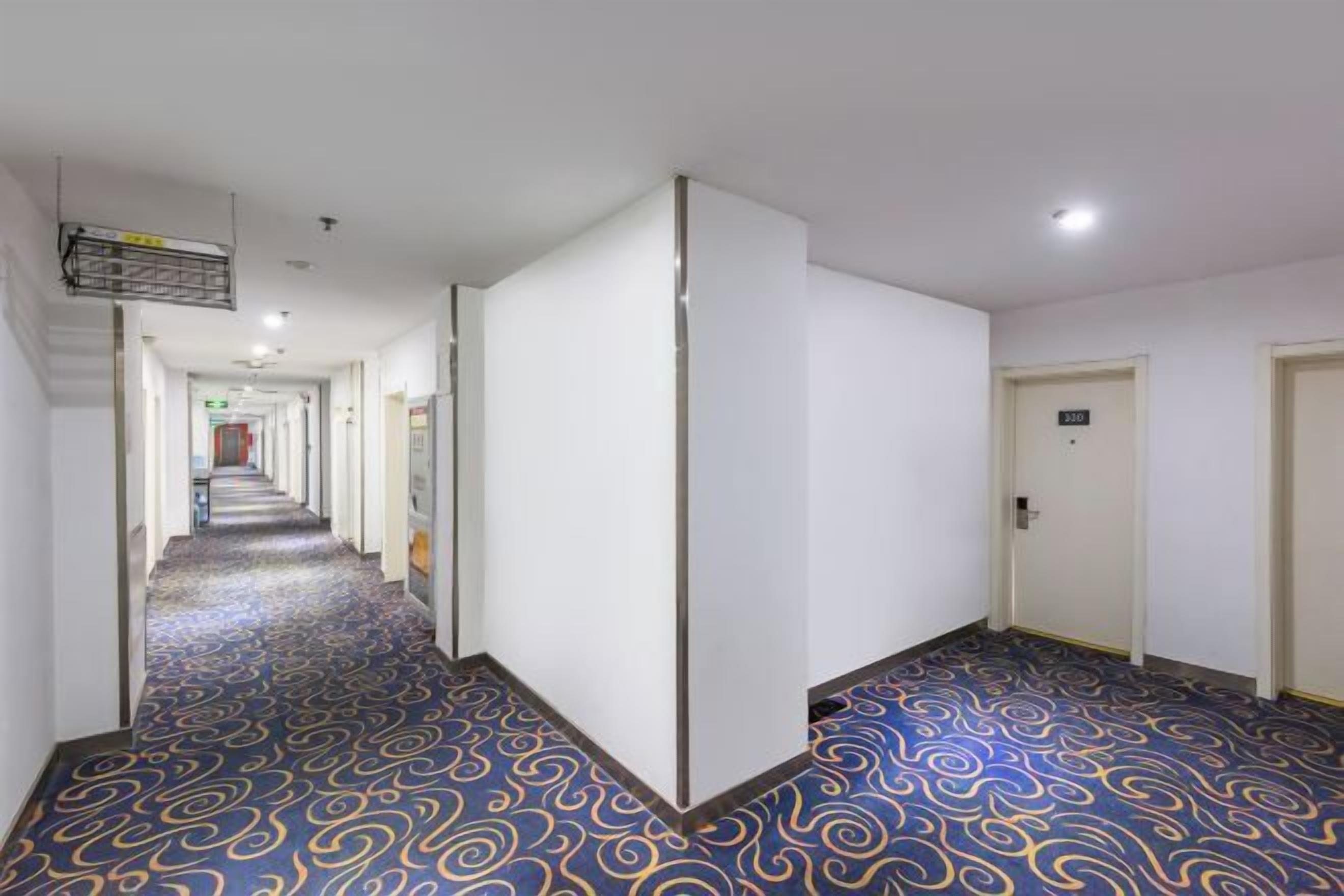 A hotel corridor with a patterned carpet, white walls, and doors leading to rooms.
