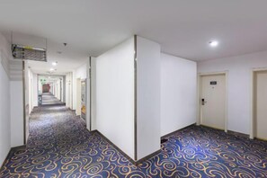 A hotel corridor with a patterned carpet, white walls, and doors leading to rooms. - 7 Days Inn Tianjin Jintang Main Road Pipe Company Light Rail Station (Tianjin)