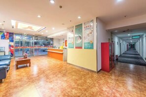 A hotel lobby with a reception desk, seating area, and a corridor leading to other rooms.