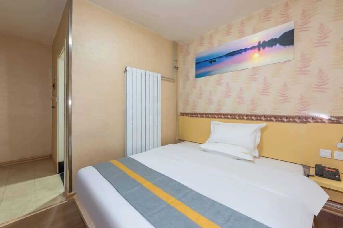 A hotel room with a bed, a radiator, a painting on the wall, and a telephone on the nightstand.