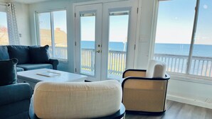 A modern living room with a view of the ocean, featuring a sofa, two wicker chairs, and a coffee table. - Panoramic Cape Cod Bay Views with Private Sandy Beach (Plymouth)