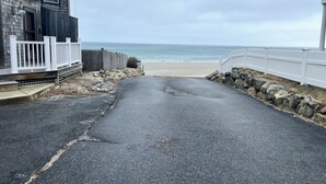 A coastal road leading to a beach with a wooden house on the left and a white fence on the right. - Panoramic Cape Cod Bay Views with Private Sandy Beach (Plymouth)