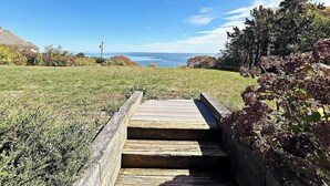 A wooden staircase leading to a grassy area with a view of the ocean. - Panoramic Cape Cod Bay Views with Private Sandy Beach (Plymouth)