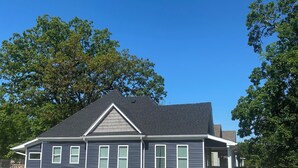 Une maison à deux étages, avec une façade bleu foncé, des boiseries blanches et une clôture en bois peinte en blanc.