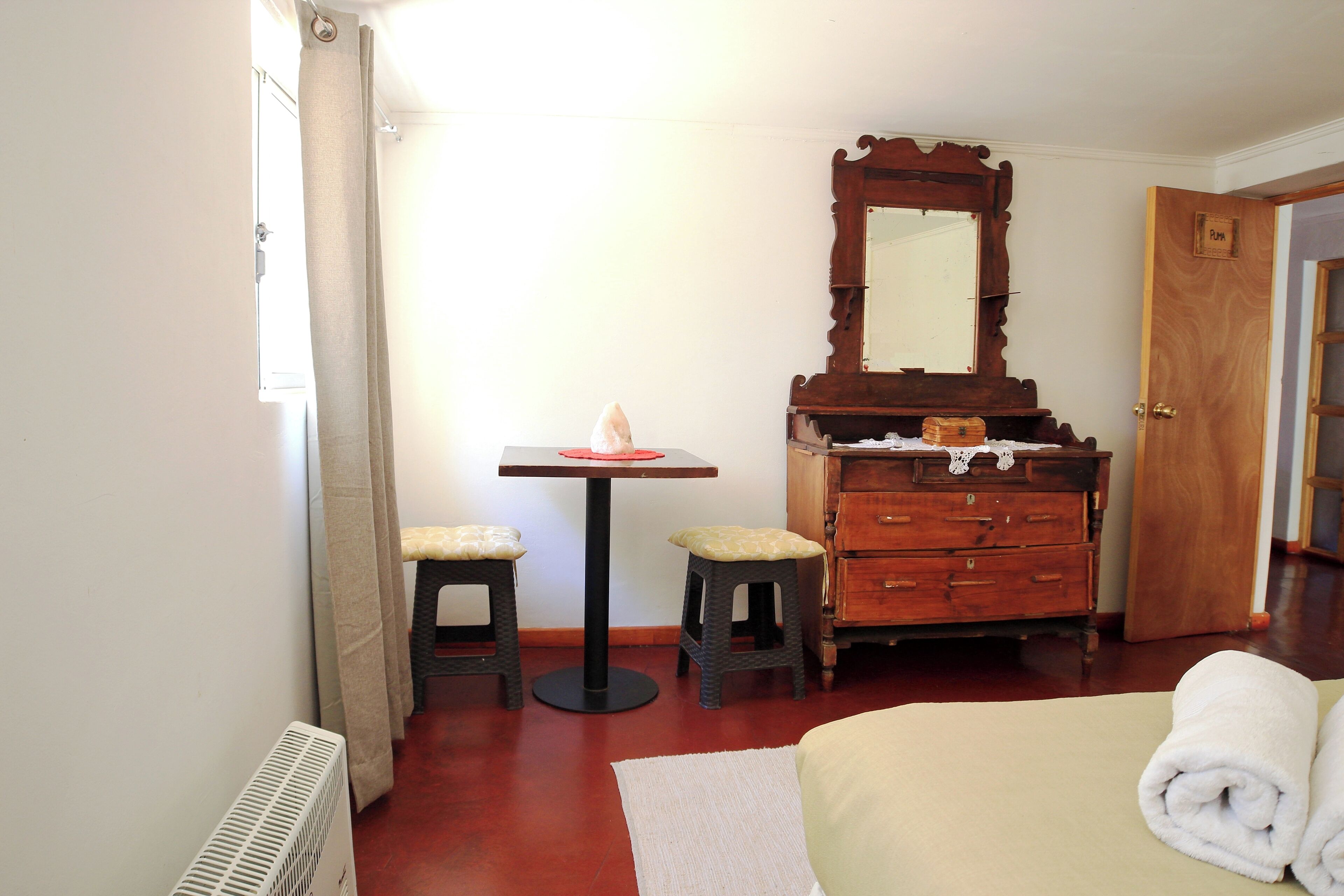 A bedroom with a bed, a wooden dresser, a mirror, and a small table with a chair.