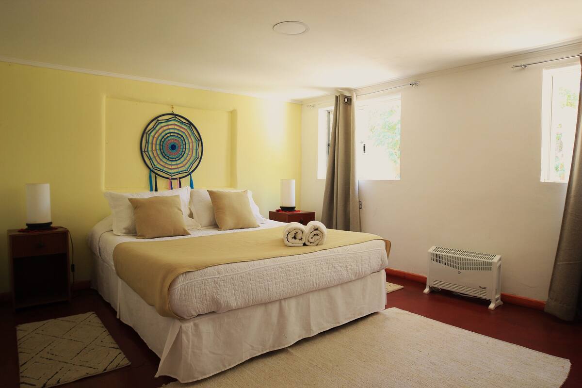 Un lit bien fait, avec une couverture et des oreillers de couleur beige, une décoration murale, une table de chevet avec une lampe et un radiateur.