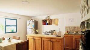 A kitchen with wooden cabinets, a gas stove, a refrigerator, and a window with blinds. - Casa Pumagui (Vicuña)