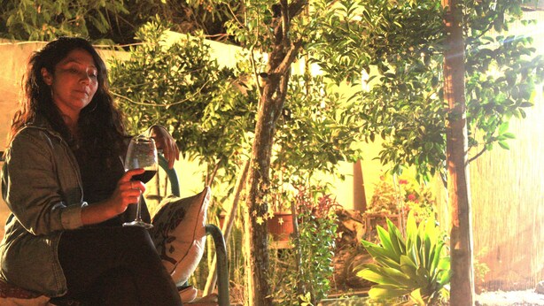 A person sitting outdoors with a glass of wine, surrounded by greenery and trees. - Casa Pumagui (Vicuña)