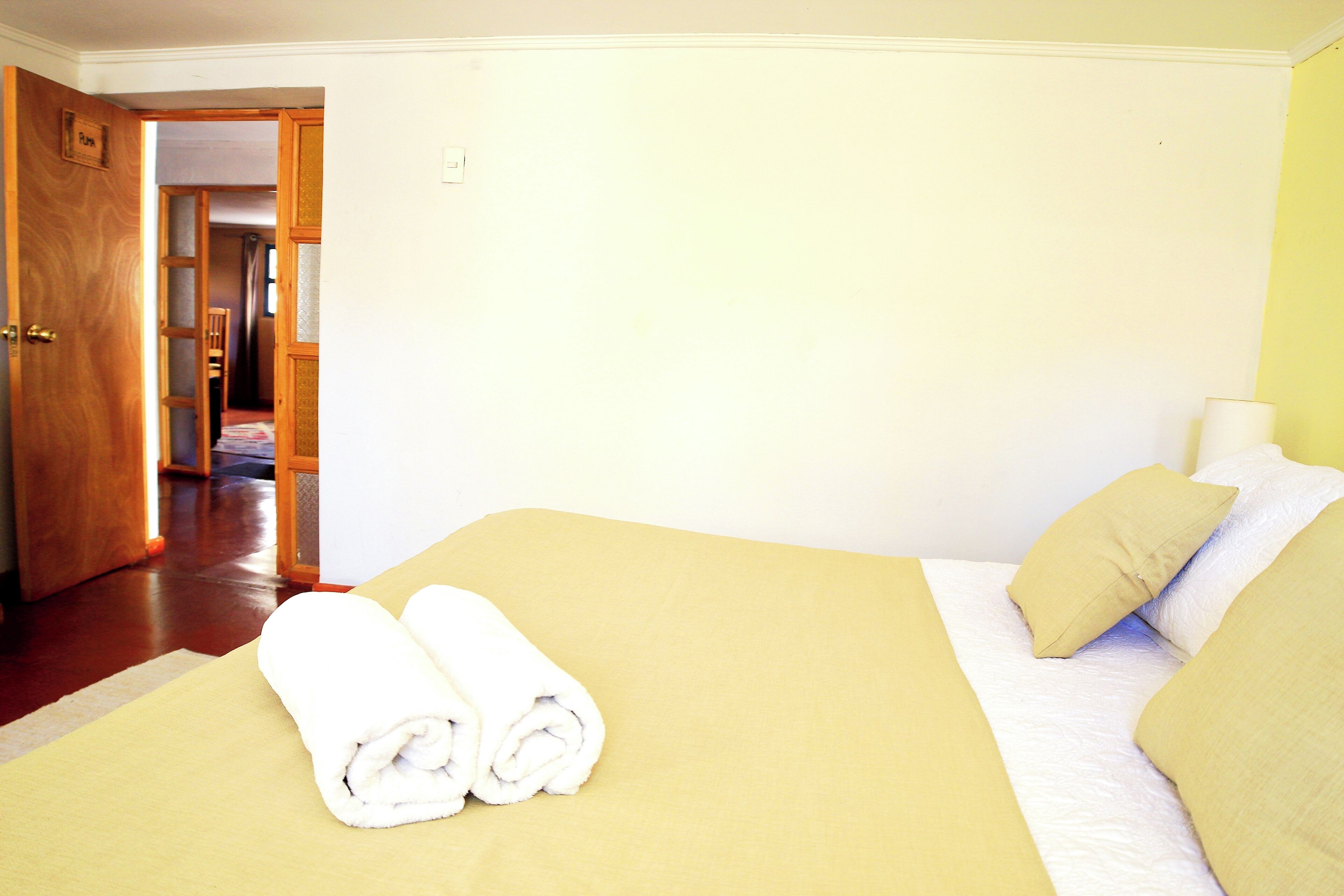 A hotel room with a bed, two pillows, and a pair of rolled towels on the bed.